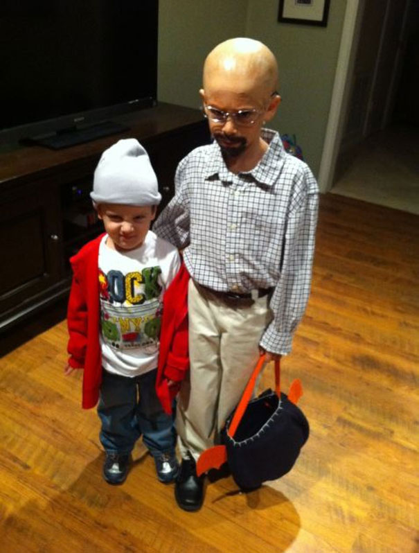Two kids in creative Halloween costumes, one dressed as a bald character with glasses, the other in a red jacket and beanie.