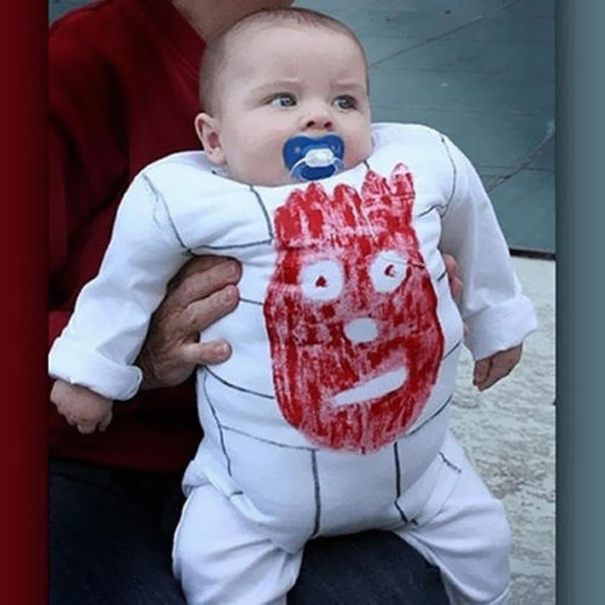 Baby in a creative kids' Halloween costume, featuring a hand-drawn red face on a white outfit, held by an adult. Baby in a creative kids' Halloween costume, featuring a hand-drawn red face on a white outfit, held by an adult.