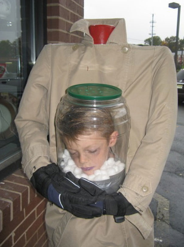 Kid in headless Halloween costume, wearing a coat and holding a jar with his head inside, showcasing creative costume ideas. Kid in headless Halloween costume, wearing a coat and holding a jar with his head inside, showcasing creative costume ideas.