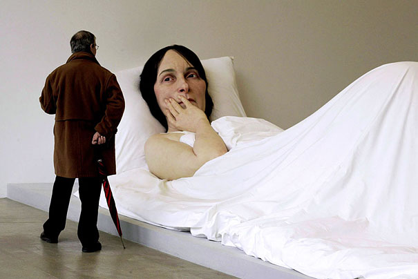 Visitor admiring hyper-realistic artwork of a giant reclining woman in a gallery. Visitor admiring hyper-realistic artwork of a giant reclining woman in a gallery.