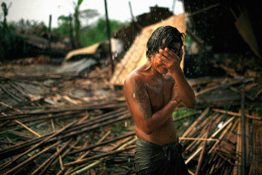 A man standing in the rain, covering his face, surrounded by debris, depicting a powerful emotional moment. A man standing in the rain, covering his face, surrounded by debris, depicting a powerful emotional moment.
