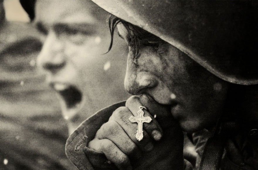 Soldier holding a cross near his lips, with an intense expression, showcasing powerful imagery and emotion. Soldier holding a cross near his lips, with an intense expression, showcasing powerful imagery and emotion.