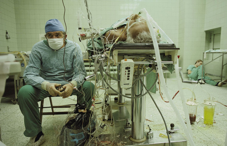 Surgeon in scrubs and mask sitting near patient surrounded by medical equipment, depicting powerful image of dedication. Surgeon in scrubs and mask sitting near patient surrounded by medical equipment, depicting powerful image of dedication.